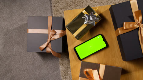 Fotografía-Cenital-De-Regalos-Envueltos-O-Regalos-En-La-Mesa-De-Casa-Con-Un-Teléfono-Móvil-De-Pantalla-Verde